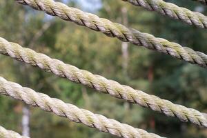 several rows of braided ropes diagonally against green foliage of trees, textured background,part of a fence, railing for climbing stairs photo