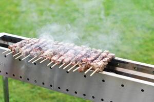 a young man grills meat kebabs on coals, ARROSTICHINI - typical southern Italian cuisine, a luxurious picnic on the terrace near the house in the summer, aromatic smoke rises above the barbecue, photo