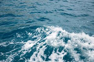 Wave on blue water and white foam on the tops of the waves from under the side of a floating boat, space for text photo