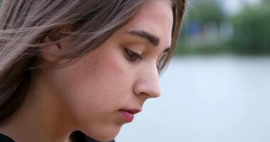face of a young girl against the background of a river, lowered down, looking at a mobile phone, reading the news, spending more time on gadgets than nature, dependence on gadgets video