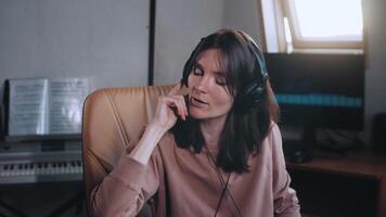 A beautiful girl with headphones listens to music in a chair at the computer, dances, looks at the camera and smiles, the equalizer is playing on the monitor. Shakes his head to the rhythm and beats. video