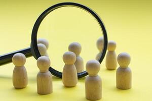 Magnifying glass surrounded by wooden figures representing searching for the right candidate. Business concept photo