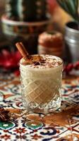 A creamy cinnamon Mexican cocktail in a clear glass on a colorful tiled tabletop. Vertical banner photo
