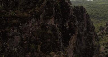 A drone flies around a young athletic female climber hanging on one arm on a belay on a steep cliff video