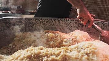 The chef stirs steaming rice in a large pilaf cauldron with a slotted spoon video