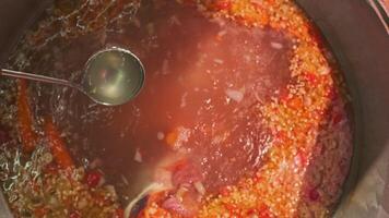 Chef mixes meat soup with vegetables in a large cauldron with a slotted spoon video