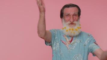 Senior man smiling friendly at camera and waving hands gesturing hello or goodbye, welcoming video