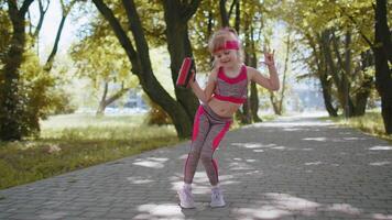 Sport runner jogger child girl listen bluetooth music speaker dancing to camera having fun in park video