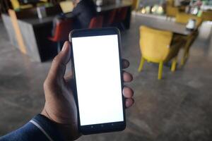 A person is holding a smartphone that has a blank screen while sitting in a modern cafe setting photo
