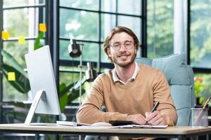 Portrait of successful financier at work at workplace inside office, mature man smiling and looking at camera, businessman in shirt working with documents graphs and charts, paperwork using laptop photo