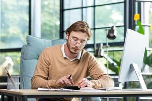 Accounting, audit. A young man works with documents and bills in the office. Calculates and checks reporting, balance, and budget on a calculator. photo