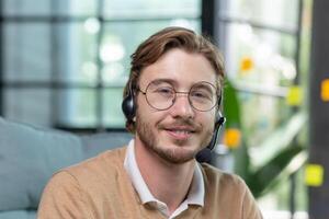 Close-up photo. Portrait of a young man in a headset and glasses, smiling and looking at the camera. photo