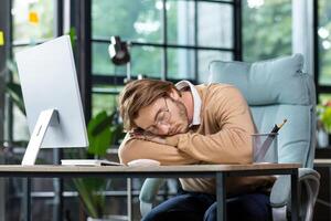 Tired programmer, IT specialist fell asleep at the workplace in the office, at home on the table in front of the computer. Overtime, deadline, project. photo