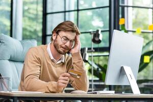 Problem with credit card, bank account. Office worker or freelancer sitting at his desk, tired of working on computer, overworked, having headache, need rest and break. photo