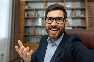 First person view of cheerful adult man in glasses having call with happy facial expression on luxury interior background. Excited office worker presenting new workplace with toothy smile. photo