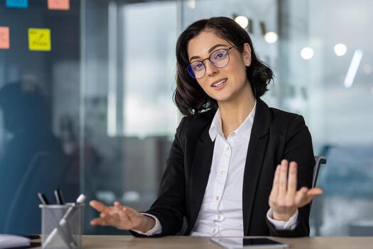 Businesswoman serious talking in call meeting, explaining concepts or strategies. Professional setting with modern glass office background. Discussing issues or conducting interview. photo
