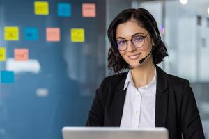 Smiling woman wearing headset working in modern office setting. Professional call center representative providing customer support, surrounded by colorful sticky notes. photo