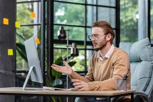 Frustrated and upset businessman reading news online from computer monitor, young blond man sad at workplace inside office in casual clothes unhappy with results. photo