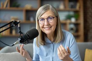 Smiling senior woman recording podcast from home studio. Enthusiastic mature podcaster sharing knowledge and experiences. Comfortable and professional setup. Engaging content creation communication. photo