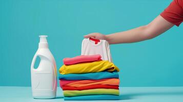 A white laundry detergent bottle, next to it there are hands of a woman placing a folded shirt. photo