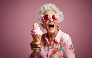 An elegant older woman, adorned with stylish sunglasses, enjoys a moment of indulgence as she savors ice cream, creating a vibrant and modern image against an isolated pink background photo
