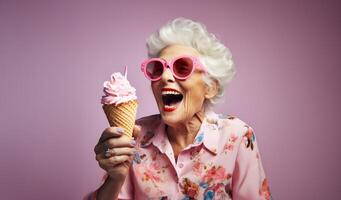An elegant older woman, adorned with stylish sunglasses, enjoys a moment of indulgence as she savors ice cream, creating a vibrant and modern image against an isolated pink background photo