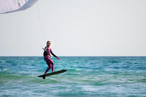 Young Caucasian woman athlete ride on a hydrofoil board with a kite in the open ocean. Hydrofoil is a new direction in kitesurfing photo