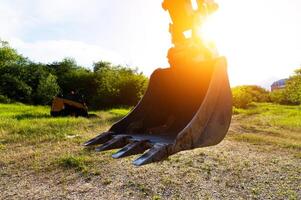 Close-up of an excavator bucket against the background of the setting sun. Excavator equipment earthworks concept photo