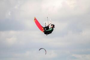 kitesurfer rides the waves at his home spot in the bay. An athlete in a panama hat performs a trick in the air while flying up against the background of a cloudy sky photo