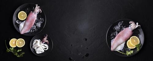 Fresh raw squid. Raw squid on a black plate with ice. Lemon slices. Top view and copy space for your text. photo