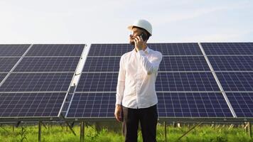 Confident engineer wearing safety hard hat, holding mobile phone, making a call. Engineer, worker, or architect working with Solar panel concept video