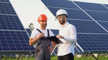 Two engineers boss and subordinate talking with each other while holding a blue print with a large solar panel in background video