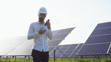 Confident engineer wearing safety hard hat, holding mobile phone, making a call. Engineer, worker, or architect working with Solar panel concept video
