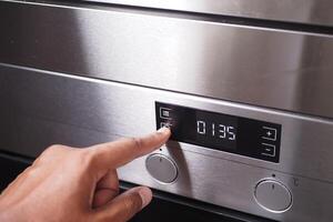 A hand is using a finger to activate the timer button on the control panel of a stainless steel oven photo