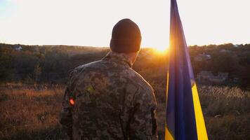 Male ukrainian army soldier stands with national banner against background of beautiful sunset. Young man in camouflage uniform with Ukraine flag as symbol of victory against russian aggression photo