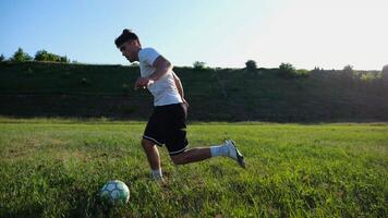 Professional footballer in uniform shows tricks with ball while running at green field. Sportsman kicks ball during jogging at meadow on sunny day. Young man training at stadium. Freestyle football photo