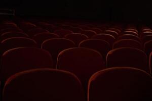 Close up of orange, red seats in dark empty cinema hall with copy space. Background with rows of chairs with selective focus. Concept of event, theatre, conference, show, presentation, audience photo