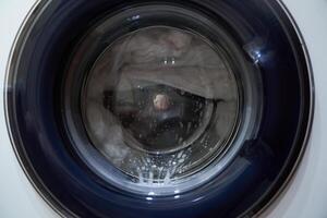 Wet white laundry in the drum of the washing machine. Close-up glass door from the washing machine with space for copying.The concept of the all-seeing eye. The picture looks like an eye. photo