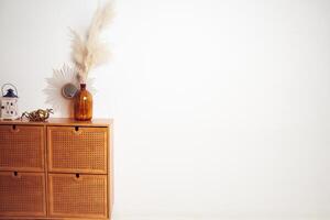 Beautiful mockup, white wall for your poster, bouquet of dried pampas grass flowers in a vase, mirror, bronze figure of beetle on drawers. Background with copy space, empty. Template for your design. photo