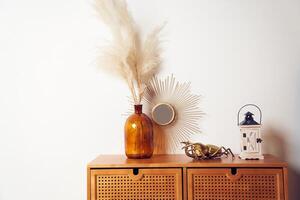 Bouquet of dried pampas grass flowers in a glass vase, mirrow, bronze figure of a beetle, wooden candle holder on brown drawers. Background with copy space, empty. Template, mockup for your design photo