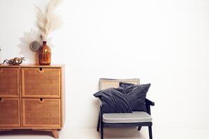 Bouquet of dried pampas grass flowers in glass vase, mirrow, bronze figure of beetle, candle holder on drawers, soft chair with pillows. Background with copy space. Template, mockup for your design photo