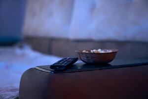 Selective focus on plate with popcorn, tv remote control, blurred view of sofa. Background, backdrop with copy space. Concept of entertainment, watching show, film, movie, news photo