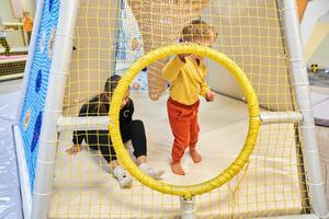 Two children on an indoor playground, unrecognizable children sitting in a maze. A modern colorful mesh playhouse for children in the mall. With space to copy photo