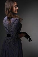 A woman with her hair down stands with her back to the camera, looking over her shoulder, in a blue retro dress in the style of the 1900s. With space to copy photo