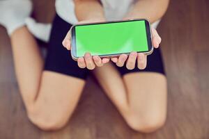 Close-up of children's hands using a phone with a green screen. A little girl is sitting on the floor and holding a smartphone with a colored key. photo