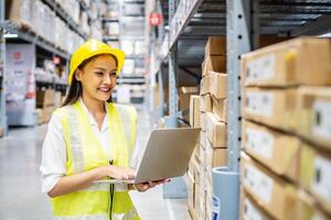 Asian engineer woman check stock details on laptop computer for checking boxes with logistics on shelves with goods background in warehouse, logistic and business export photo