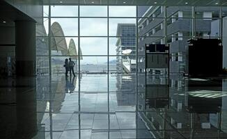 Airport terminal huge glass window with view of departure buildings and silhouette of two persons photo