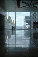 Airport terminal huge glass window with view of departure buildings and silhouette of two persons photo