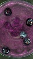 Top-down view of a vibrant purple blueberry cocktail with sparkling glitter and fresh blueberries floating on the surface, ideal for vertical shot stories on TikTok and Instagram, capturing the video