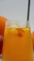 Vertical shot of a refreshing iced orange beverage with a metal straw, fresh peach slices, and ice cubes against a light background, ideal for TikTok and Instagram stories, capturing the essence of video